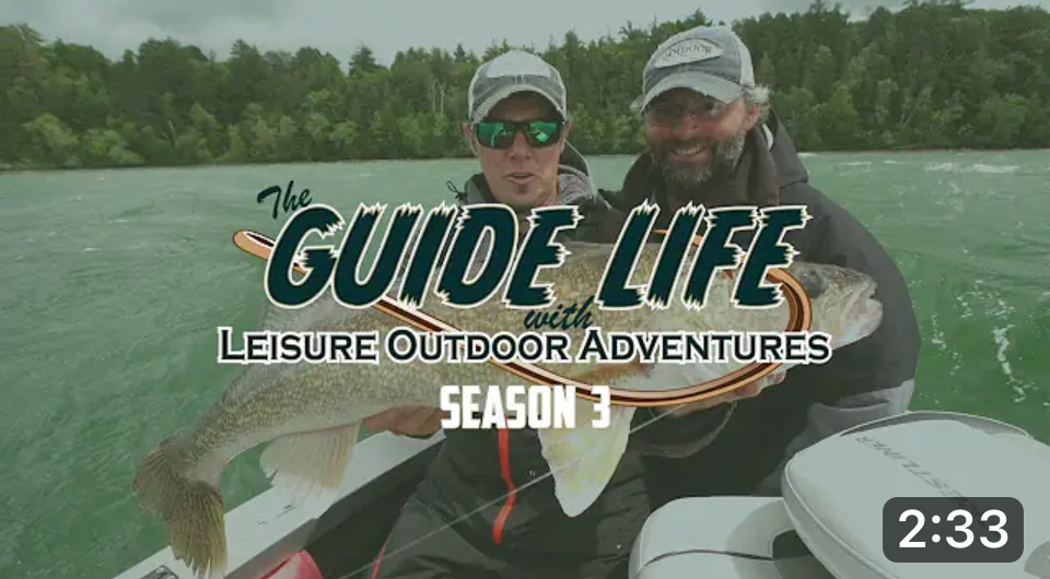 Two people in fishing gear, guided by a skilled fishing guide, hold a large fish on a boat with green water and trees behind them. Text reads “The Guide Life with Leisure Outdoor Adventures Season 3.” A 2:33 time stamp appears at the bottom right.